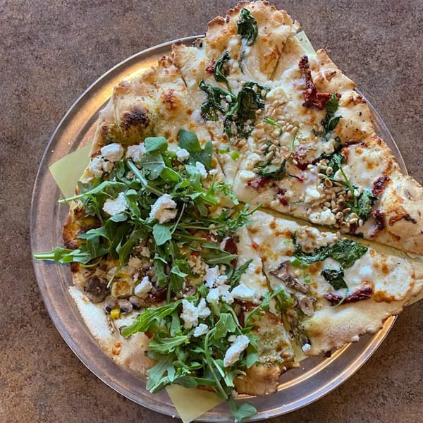 Bullman's Wood Fired Pizza with arugula, feta, mushrooms, and pine nuts on a metal tray.