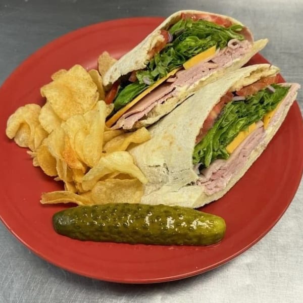 A Bullman's Wood Fired Pizza sandwich with chips and a pickle on a red plate.