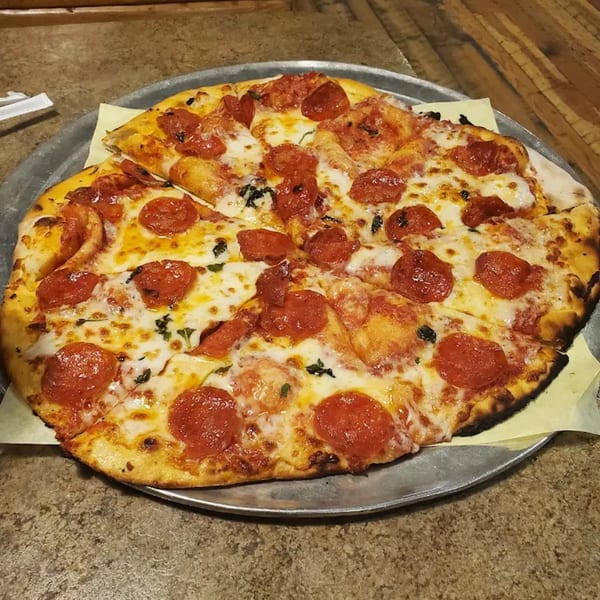 A Bullman's Wood Fired Pizza pepperoni pizza with melted cheese and basil on a metal tray.
