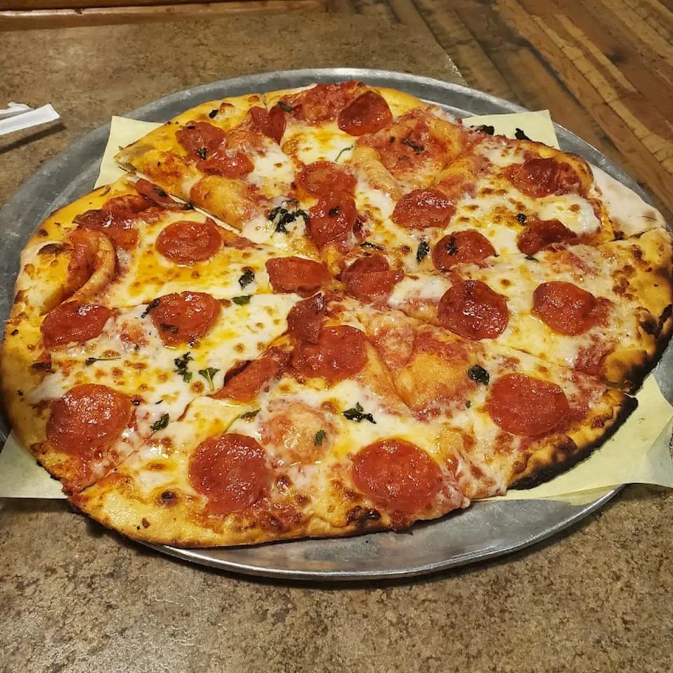 A Bullman's Wood Fired Pizza pepperoni pizza with melted cheese and basil on a metal tray.